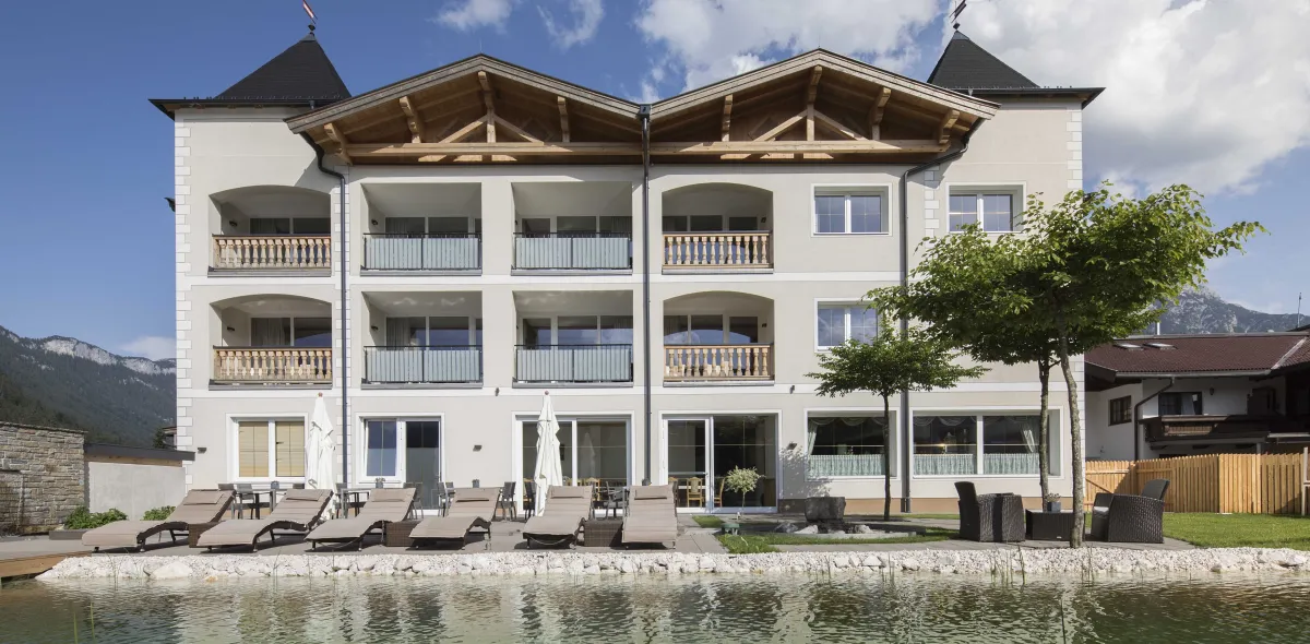 Schwimmteich des Hotels und angrenzende Terrasse mit Sonnenliegen und Sitzbereich 