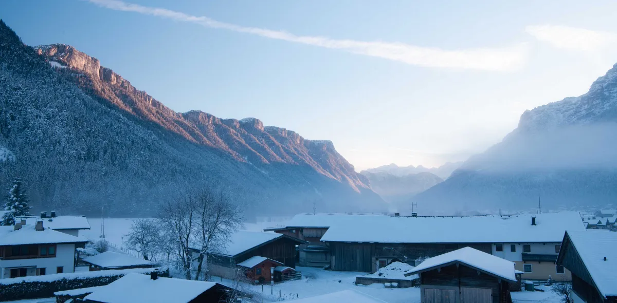 Verschneite Winterlandschaft und Häuser vor Bergen im Sonnenuntergang