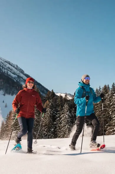 Mann und Frau bei Schneeschuhwanderung mit Berg und Wald im Hintergrund